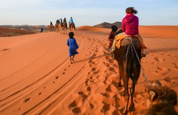 Couple riding camels at sunset in Merzouga Sahara Desert during a multi day tour from Marrakech