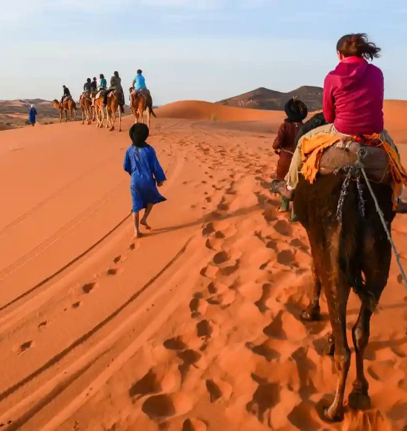 Couple riding camels at sunset in Merzouga Sahara Desert during a multi day tour from Marrakech